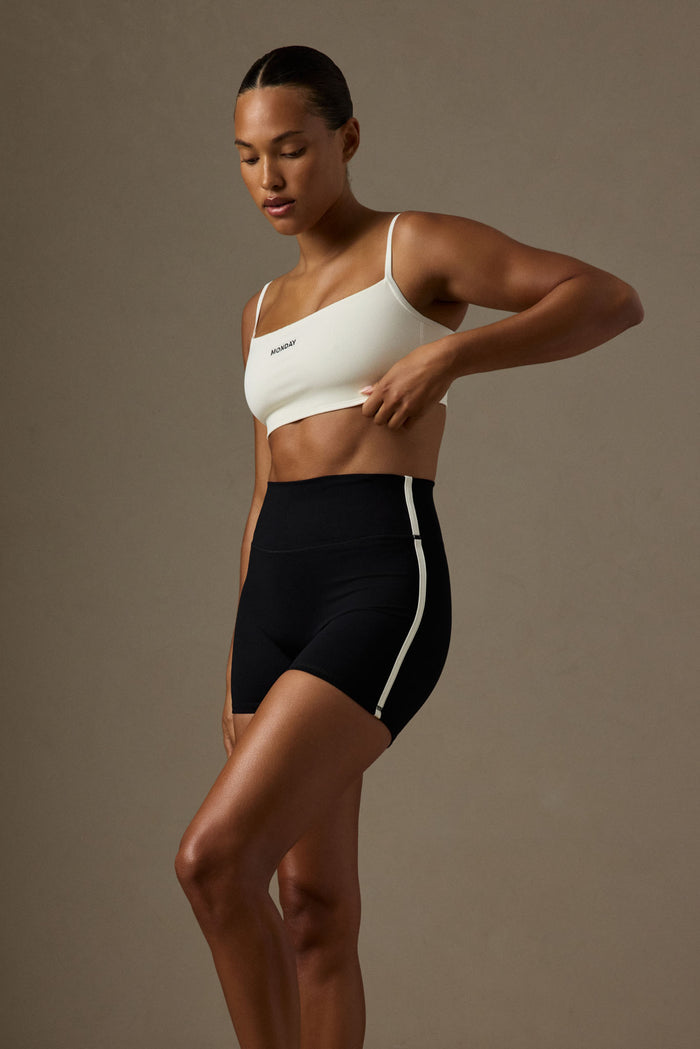 Three-quarter of Elysian Short 4.5 in black with ivory side stripe, high-waisted mid-thigh fit on model, neutral background