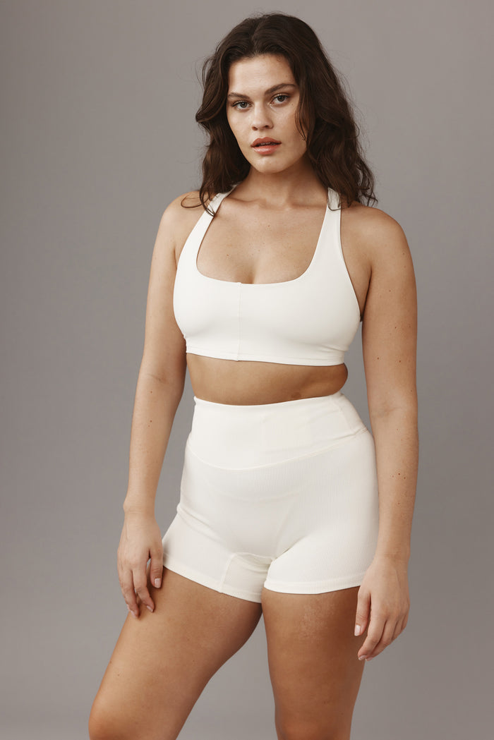 Three-quarter view of Elysian Short 4.5-inch in Ivory Lightweight Rib showcasing high-rise ribbed waistband and short inseam on model with gray background