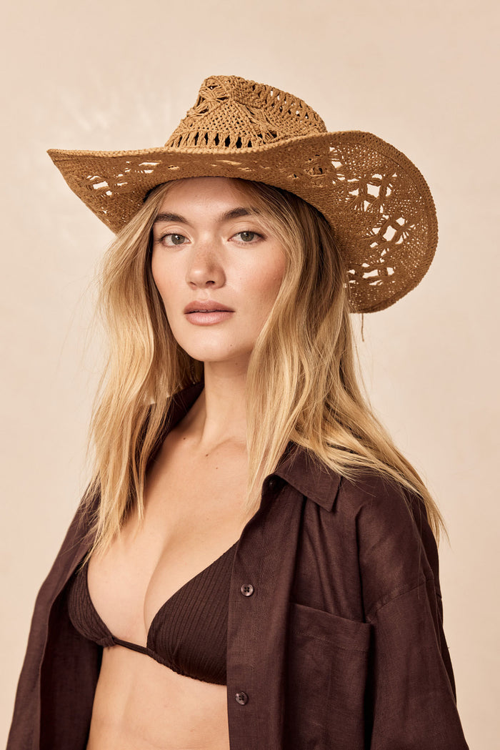 Front view of Exuma Hat in natural rattan on model showcasing open woven weave, wide brim and adjustable inner tie, neutral background