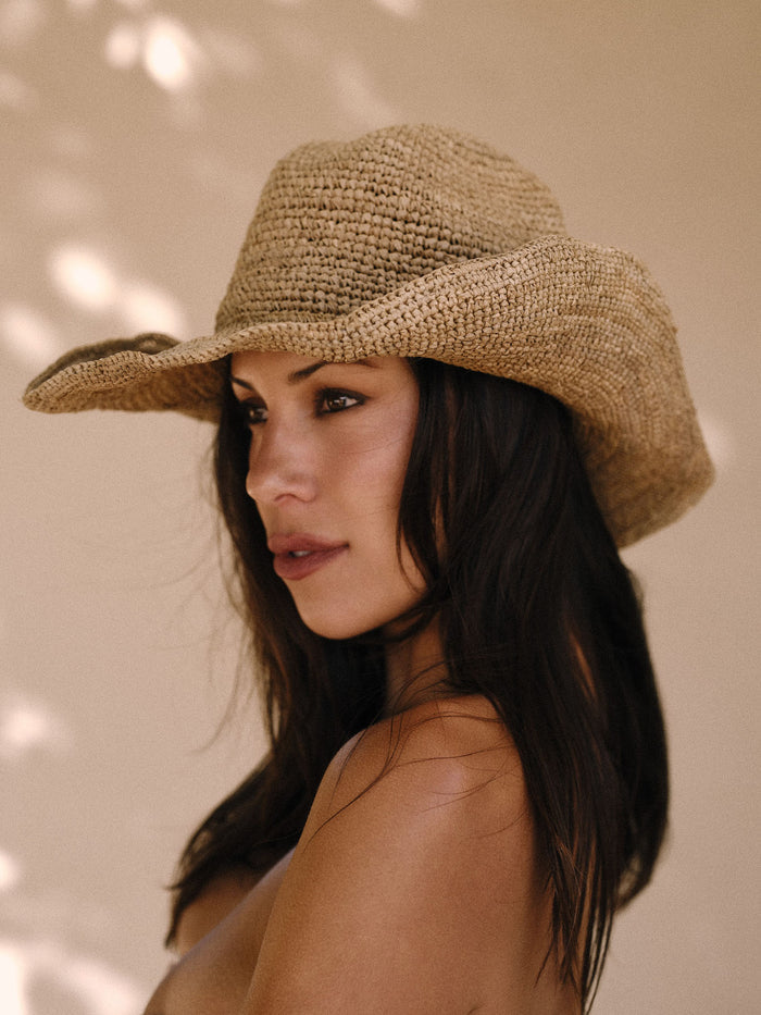 Three-quarter profile of Exuma Raffia Hat in Husk on model showcasing woven raffia straw, flexible wired brim and adjustable inner tie against a neutral beige background