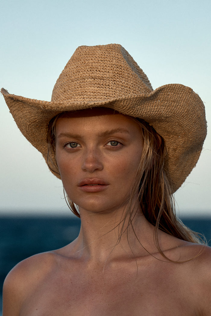 Close-up front view of Exuma Raffia straw hat showing woven flexible straw and shaped wire brim on model at the ocean