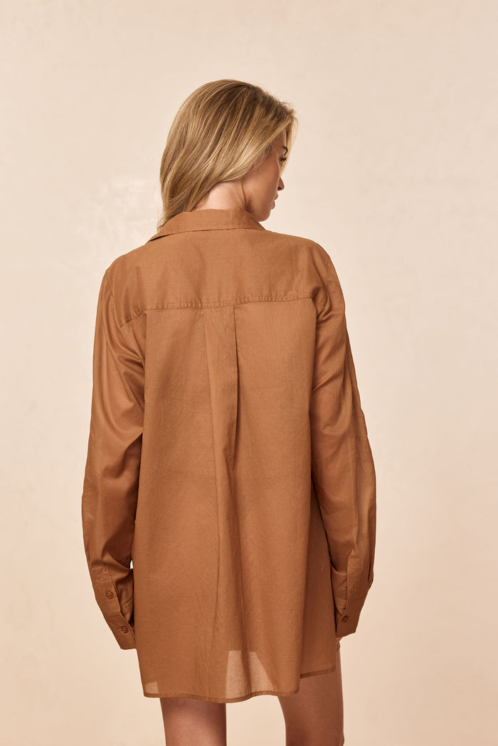 Rear view of Fiji Tunic in caramel cotton voile on model, showing center back pleat and long sleeves against a neutral background