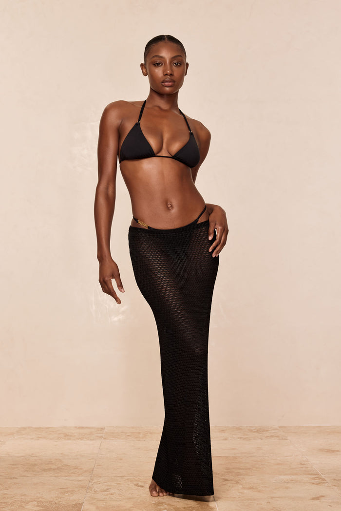 Front view of Hanalei Bottom in black showing low-rise string with thin side straps and gold hardware against beige backdrop