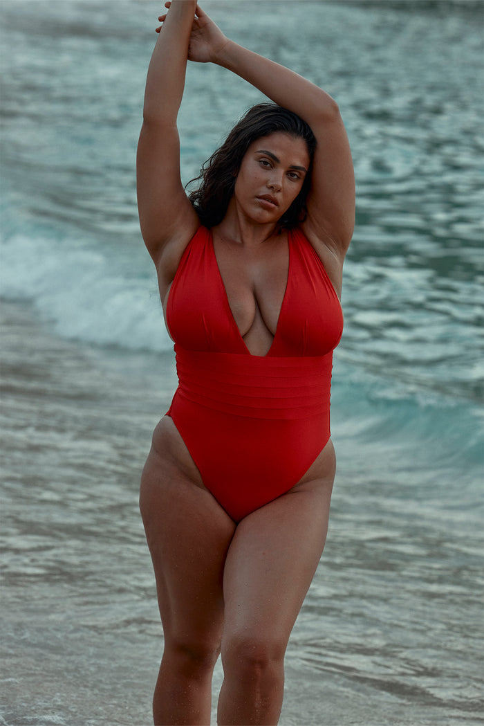 Front view of Florence One Piece in Chili Pepper showcasing deep V-neck and pleated waist, model standing waist-deep in surf