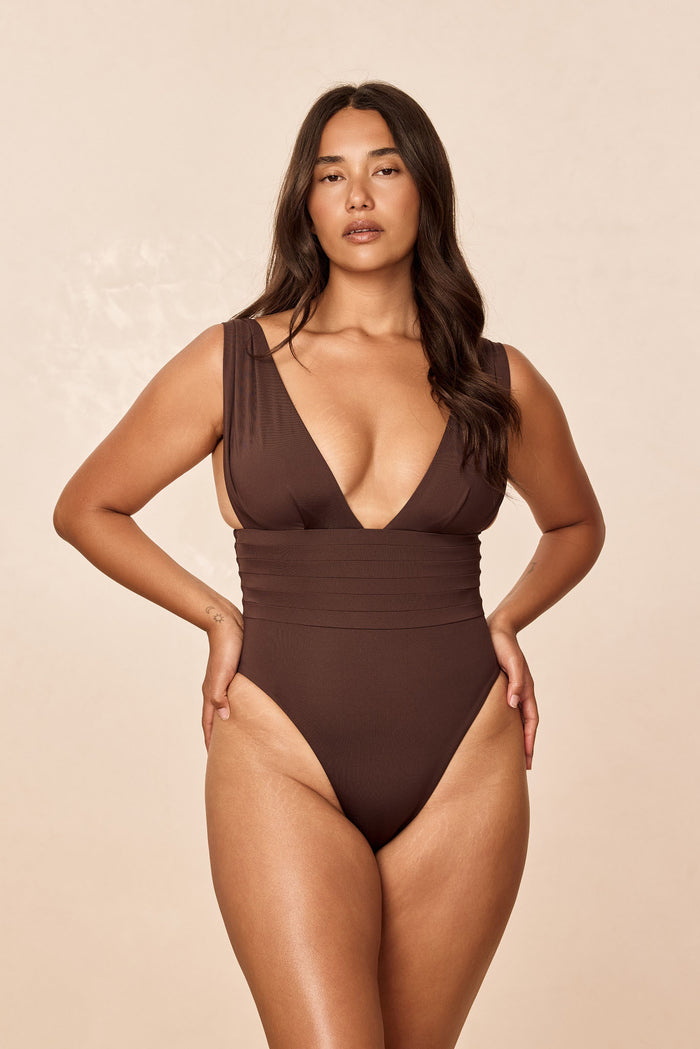 Front view of Florence One Piece in Espresso showcasing deep V neckline, pleated waist and high-cut leg on beige background