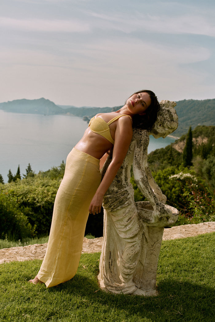 Three-quarter view of Fontelina Linen Skirt in Honey showing high-rise fitted waist and slim silhouette with sea view
