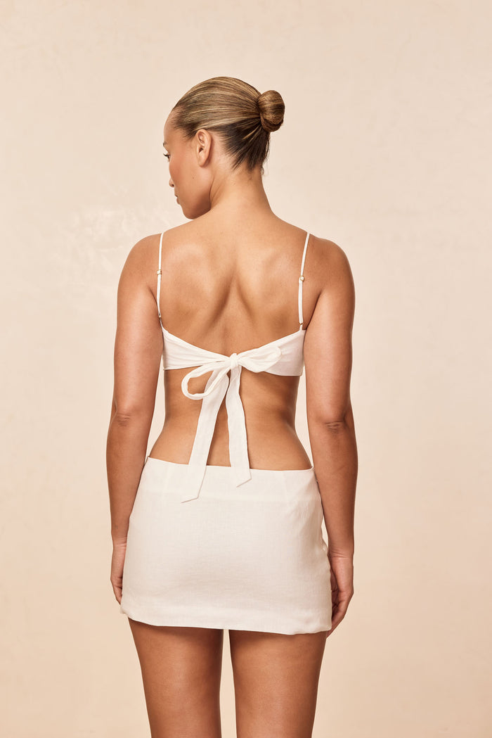 Back view of Fontelina Mini Skirt in white linen showcasing mini length and back zipper with beige studio background