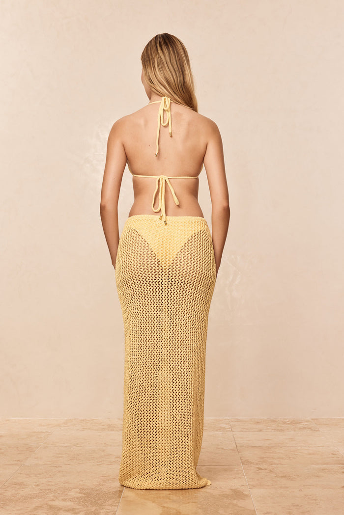 Back view of Fontelina Skirt in Honey showing open-knit crochet maxi skirt over bikini bottoms on beige background