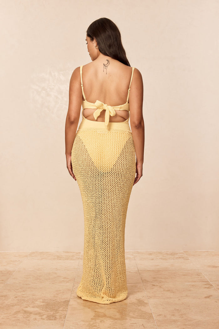 Back view of Fontelina Skirt in Honey Petit Crochet showcasing open-knit crochet fabric, tie-back waist, and maxi silhouette on model against beige studio background