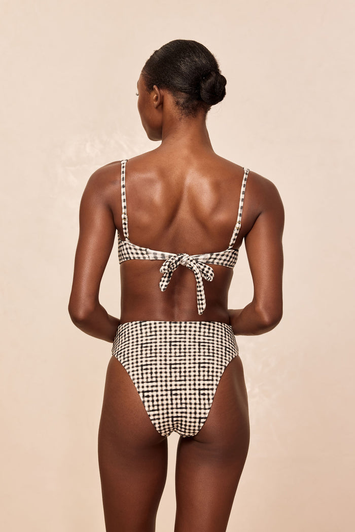Rear view of Formentera bottom in black gingham showing high‑rise fit and moderate rear coverage on beige background