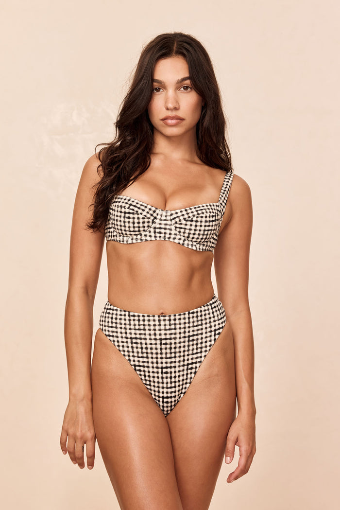 Front view of Formentera Bottom in black gingham on model showcasing high‑waist, high‑cut silhouette with beige background