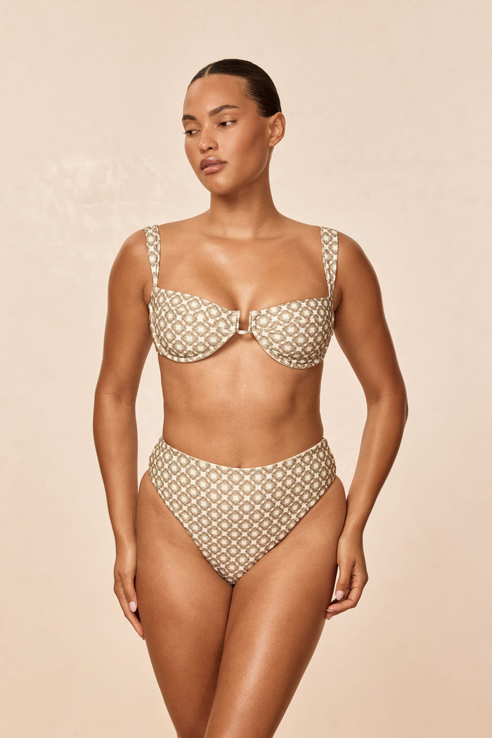 Front view of Formentera bottom in Tile Geo showing high-waist and high-cut cheeky coverage on model, beige background