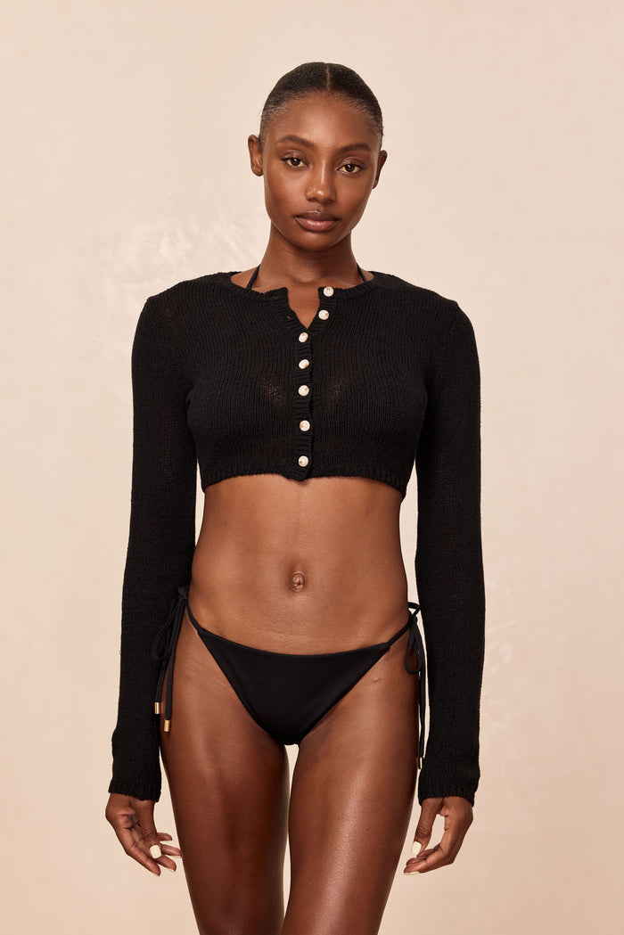 Front view of Genoa Cardigan in black open jersey, cropped button-front with long sleeves on model against beige background