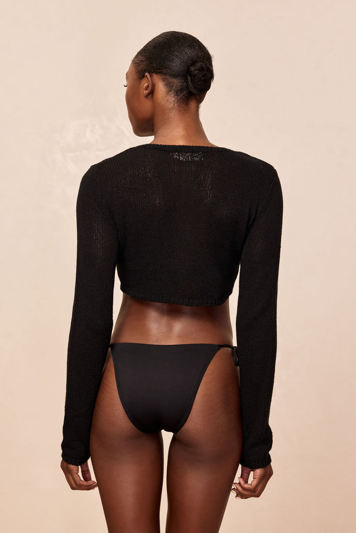 Rear view of Genoa Cardigan in black open jersey showcasing cropped hem and open-knit texture with beige backdrop