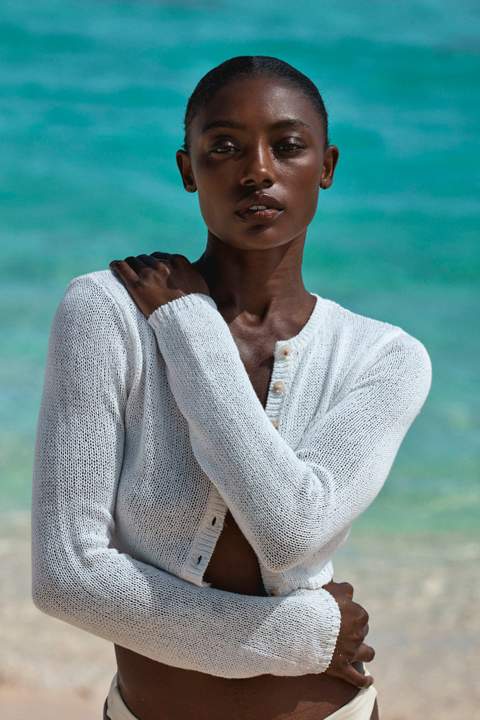 Genoa Cardigan in ivory open-knit shown front on model, cropped button-front silhouette, beach background