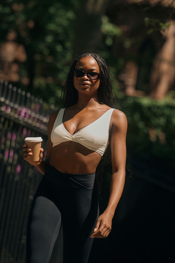 Front view of Griffith Bra in ivory showing twist-front V-neck and wide straps on model walking outdoors with coffee cup