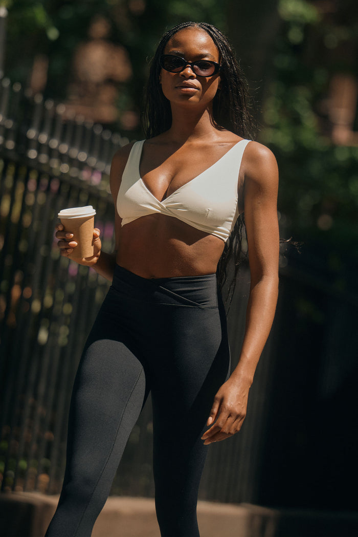 Front view of Griffith Bra in Ivory on model walking outdoors holding a coffee cup, showcasing twist-front V-neck and supportive fit