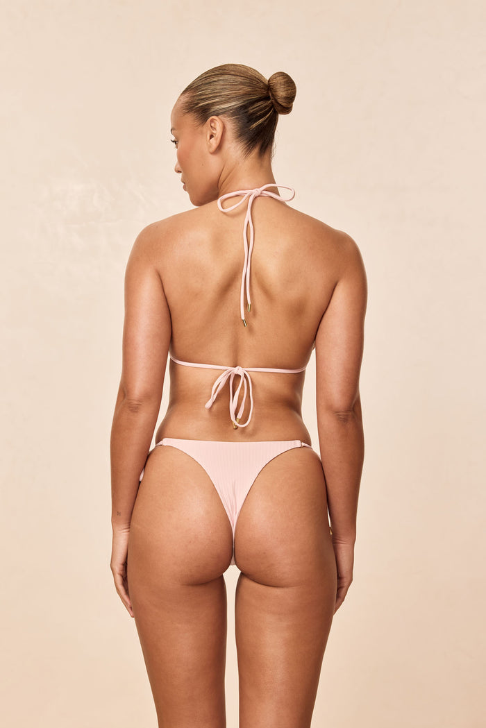 Rear view of Hanalei bottom in powder pink rib showing cheeky coverage and low-rise fit on model against beige background