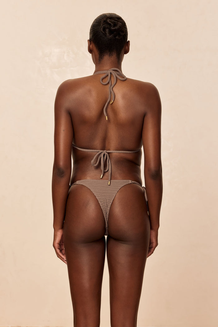Rear view of Hanalei Bottom in Stone Crinkle showcasing cheeky high-cut fit on model with neutral beige background