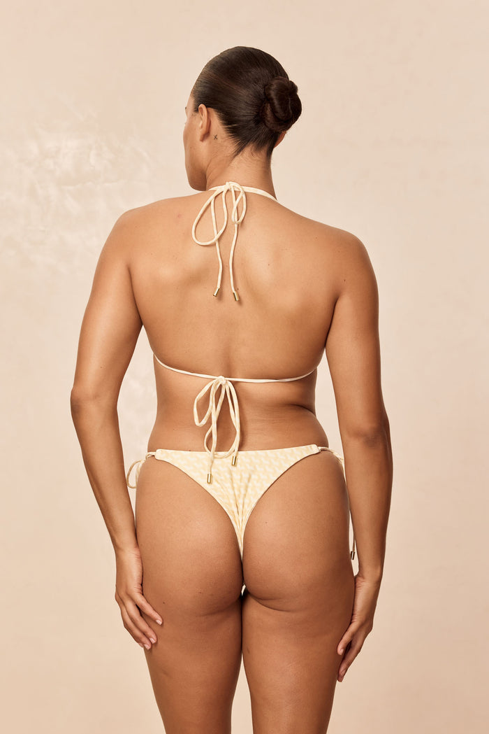Back view of Hanalei Top in Ivory Geo showing thin adjustable neck and back ties with gold hardware on beige background