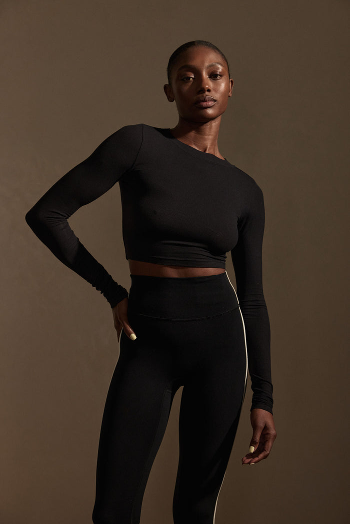 Front view of Hayworth Long Sleeve cropped black ribbed top showcasing lightweight rib texture, crew neckline, and long sleeves on model against brown backdrop