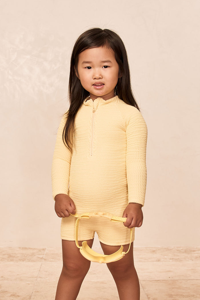 Front of Hilo One Piece Kids in Honey Crinkle with long sleeves, front zipper and crinkle texture on neutral background
