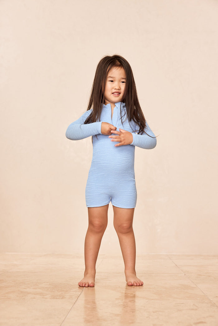 Front view of Hilo One Piece Kids Sky Crinkle showing crinkle texture, long sleeves and front zipper on beige backdrop