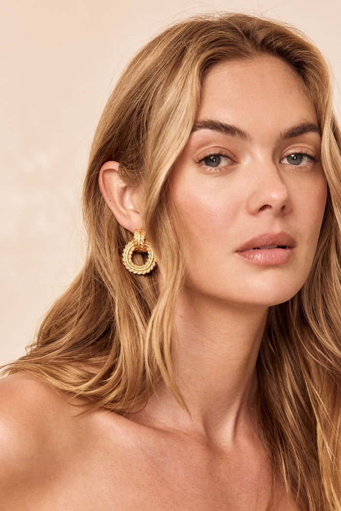 Close-up of Holbox Earrings in gold showcasing textured double-hoop chain-link design on model against a beige background