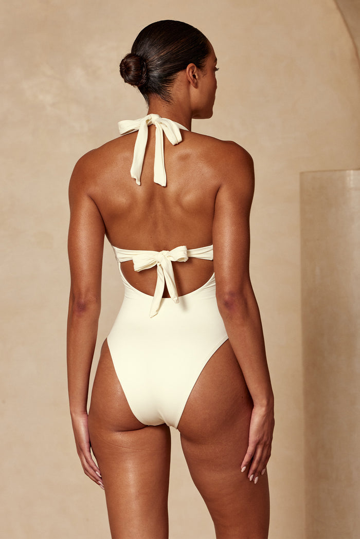 Woman seen from the back wearing a cream halter one-piece swimsuit tied in bows at neck and mid-back