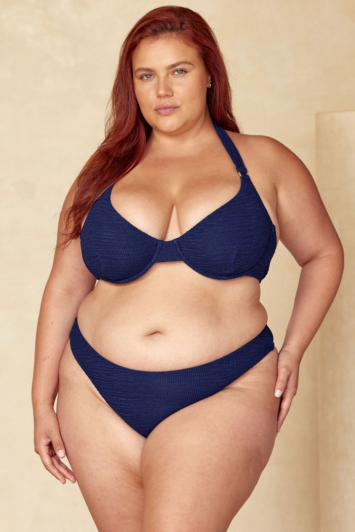 Front view of Honolulu Top Midnight Crinkle, navy textured fabric, underwire cups and halter strap on beige background