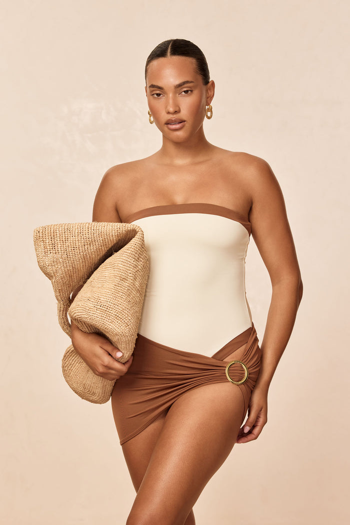 Front view of Jamaica sarong in caramel showing hip-wrap tie with gold ring, worn on model holding a straw hat against a neutral background