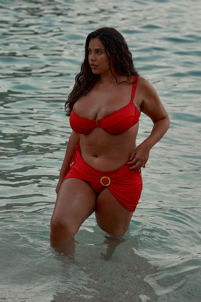 Three-quarter front view of Cala Roja Top showcasing underwire balconette cups and adjustable shoulder straps with model knee-deep in ocean water