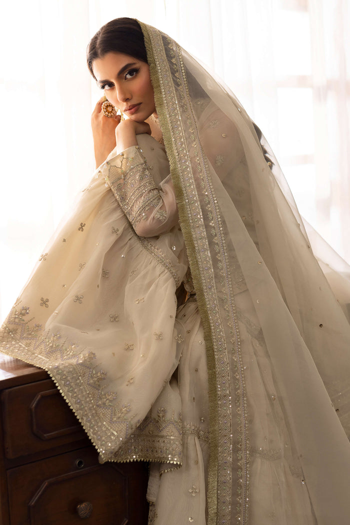 Model wearing full NAQSHI Jeena 3PC set: pearl-white organza shirt with stone boat neckline, lavender-tinged gharara, chunky tassels and embroidered sequin dupatta.