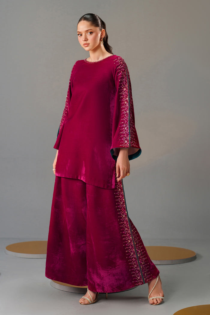 Woman wearing a magenta outfit with intricate patterns on a gray background
