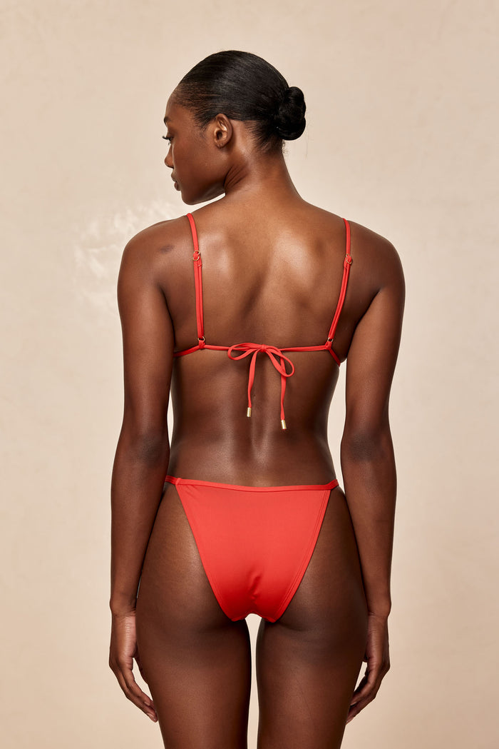 Rear view of Kauai Top in Chili Pepper showing tie-back and adjustable straps on model against beige background