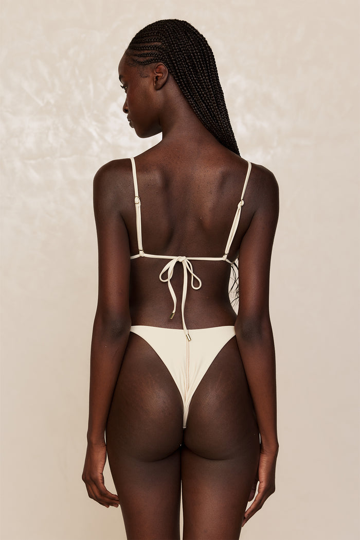 Back view of Kauai Top in Champagne Denim showcasing adjustable thin shoulder straps and tied back with gold hardware on a neutral beige background