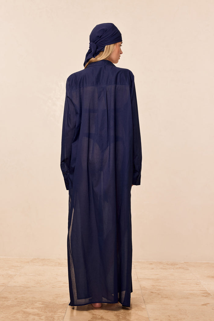Back view of Kokomo Kaftan in Midnight cotton voile showing semi sheer fabric, long sleeves and collar on a neutral beige background