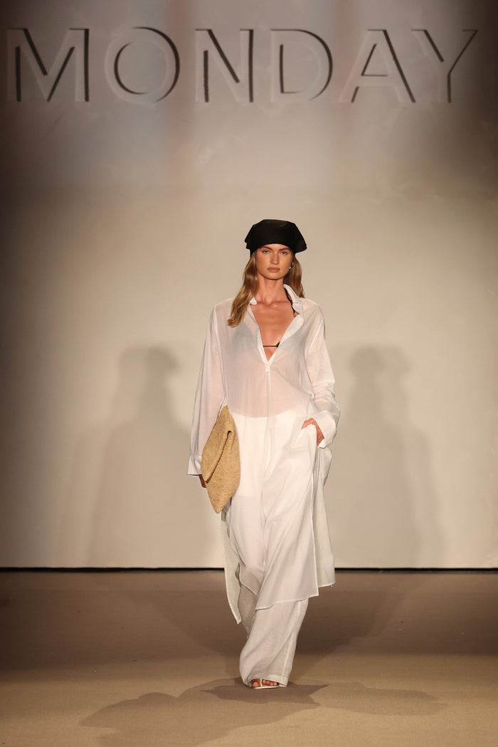 Front view of Kokomo Kaftan in white on model, semi-sheer cotton voile with pleated front, side pockets, runway backdrop