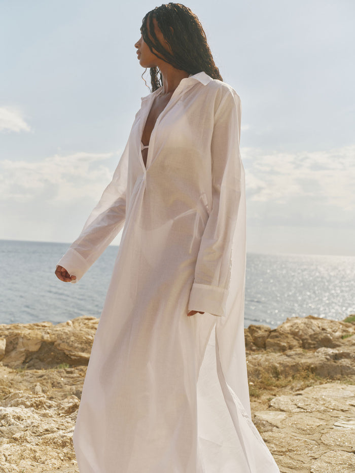 Three-quarter profile of Kokomo Kaftan maxi in white showing semi-sheer voile, pleated front and side slit at the seaside