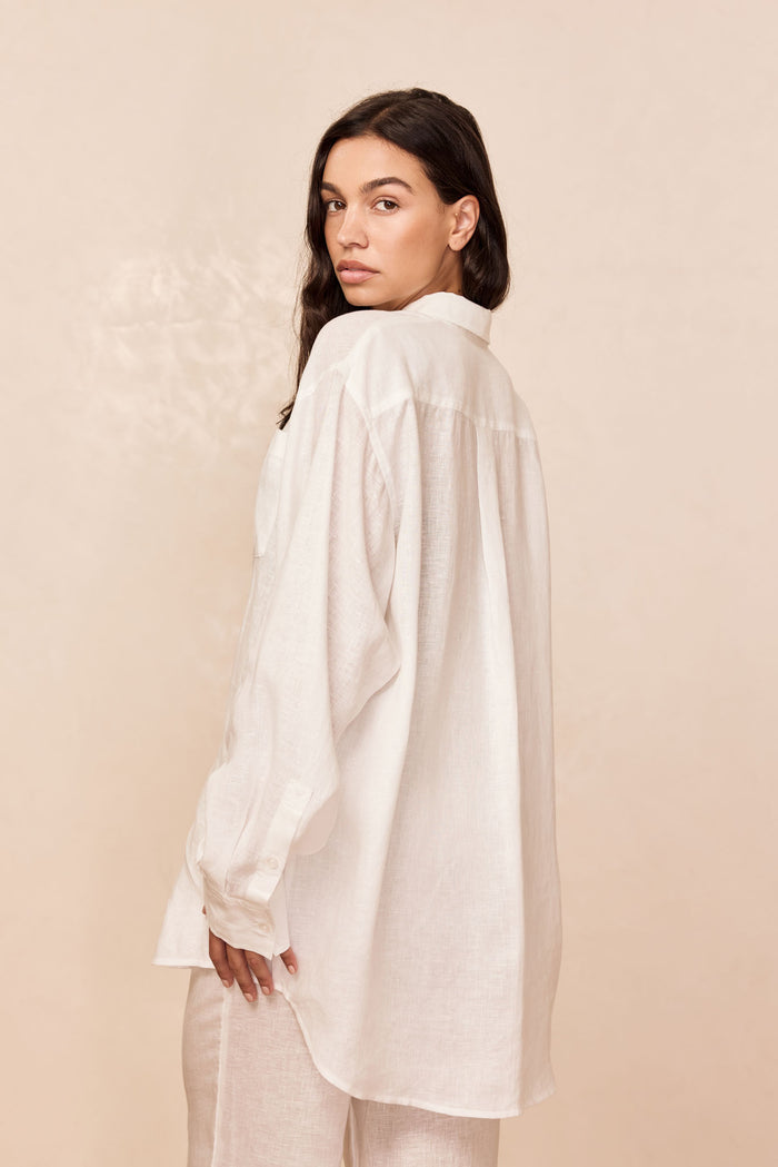 Back view of La Jolla Linen Shirt in White Linen showcasing relaxed oversized fit and curved hem on beige background