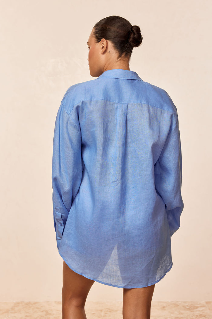 Back view of La Jolla Shirt in Azure Linen on model showing relaxed fit, long sleeves, collar and back pleat on beige background