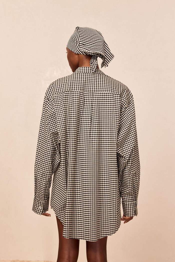 Back view of La Jolla Shirt in black gingham showcasing oversized fit, long sleeves, and shirttail hem on beige background