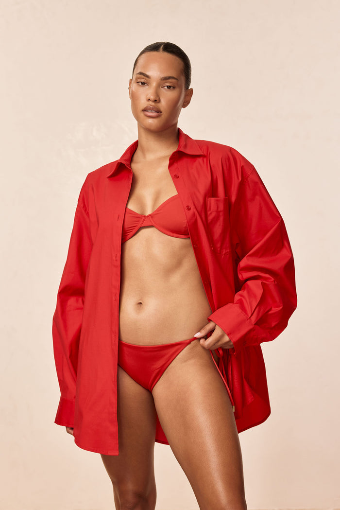 Front view of La Jolla Shirt in Chili Pepper, oversized button-down worn open over matching bikini on beige background