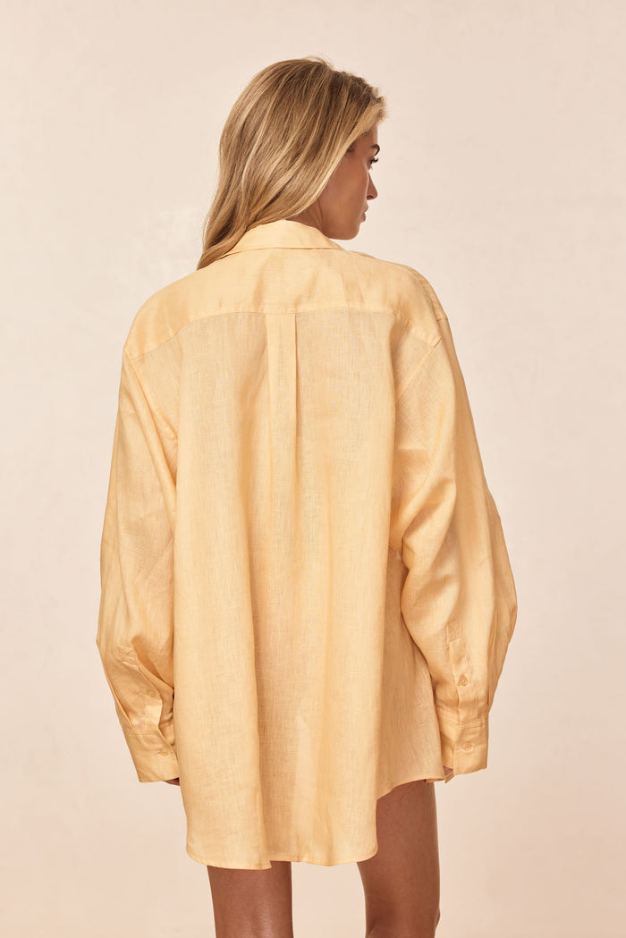Back view of La Jolla Shirt in raffia linen showing center back pleat and relaxed oversized fit on a neutral backdrop