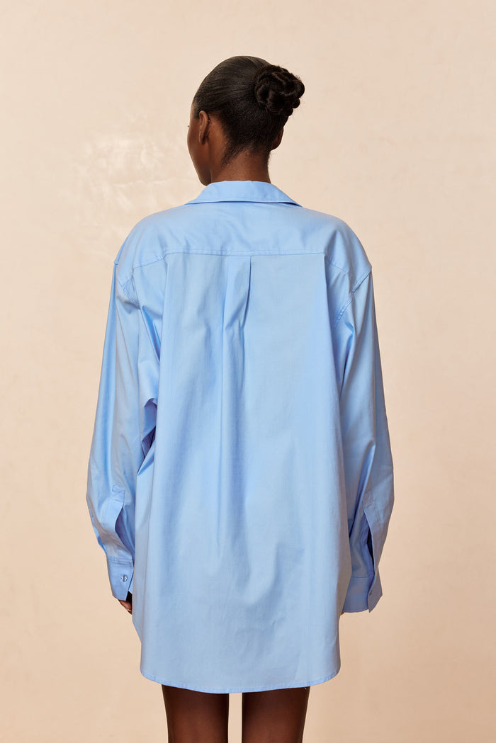 Back view of La Jolla Shirt in sky with oversized fit, box pleat back and long sleeves on beige backdrop