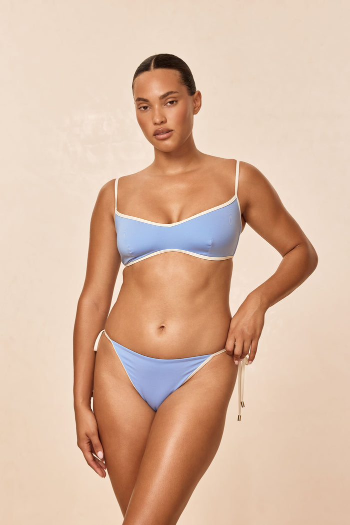 Front view of Le Marais Bottom in azure with ivory trim, tie-side low-rise bikini on model against beige studio background