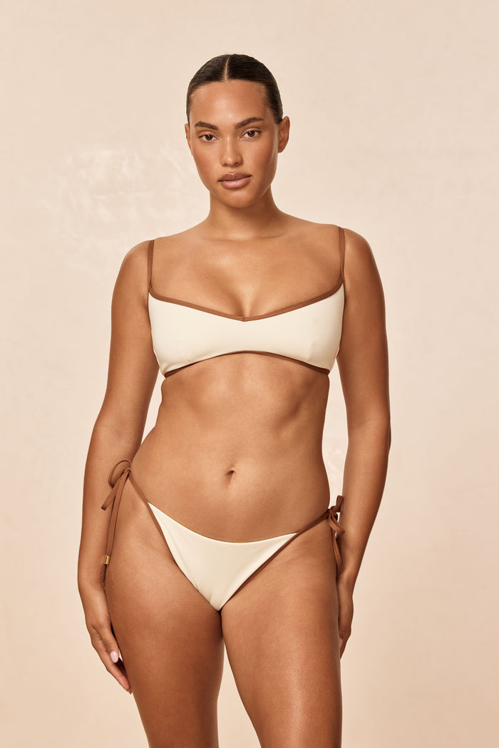 Front view of Le Marais Bottom in ivory and caramel on model showing color-block detail, adjustable tie sides with gold hardware, medium-to-cheeky coverage on beige background