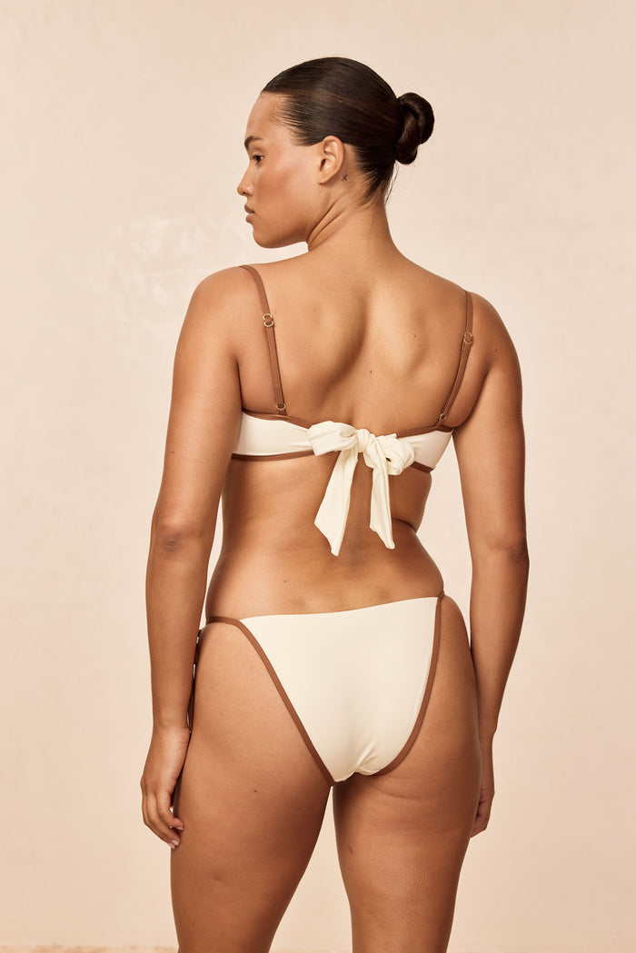 Rear of Le Marais Bottom in Ivory/Caramel showing color-block trim and medium-to-cheeky coverage on beige background