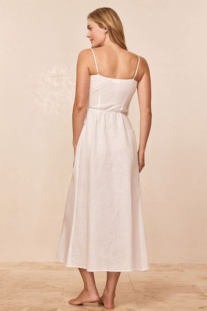 Back view of Levanzo Dress in white linen showcasing adjustable spaghetti straps and tie waist on tile floor