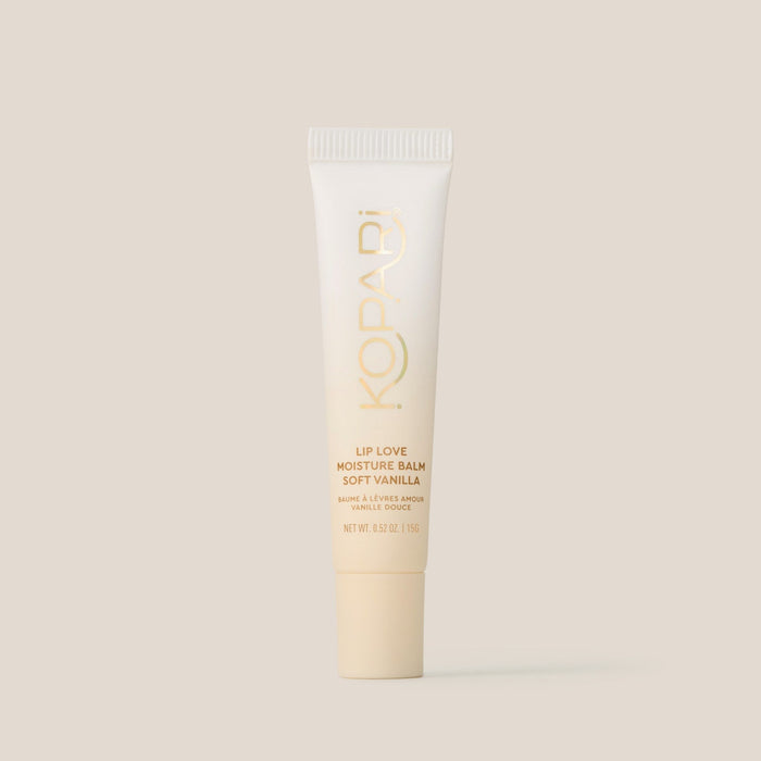 Front view of Lip Love Moisture Balm tube in Soft Vanilla showcasing gold Kopari logo and product labeling on beige background